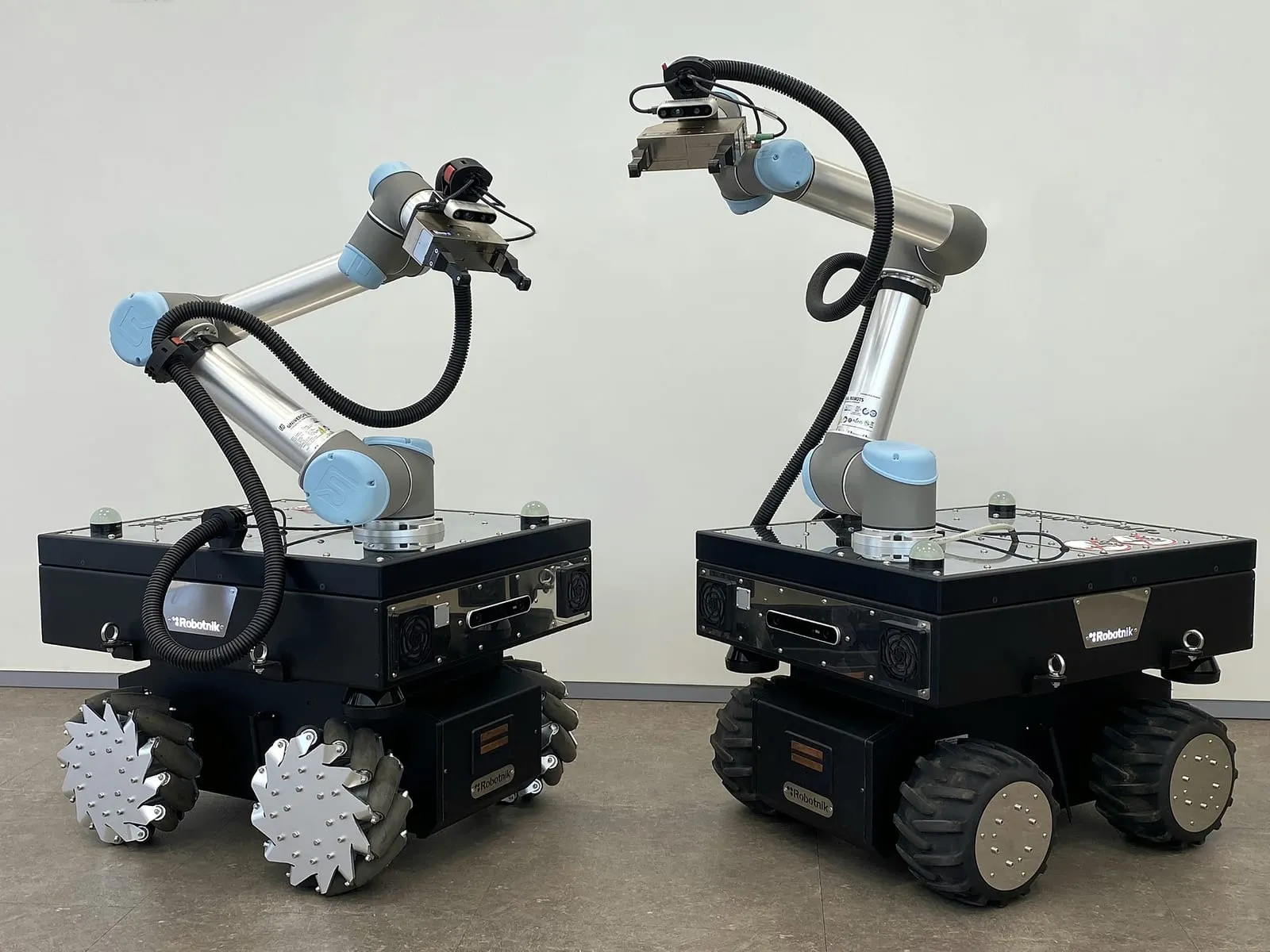 Two mobile robots carrying arms, one on mecanum wheels and one on rubber tyres